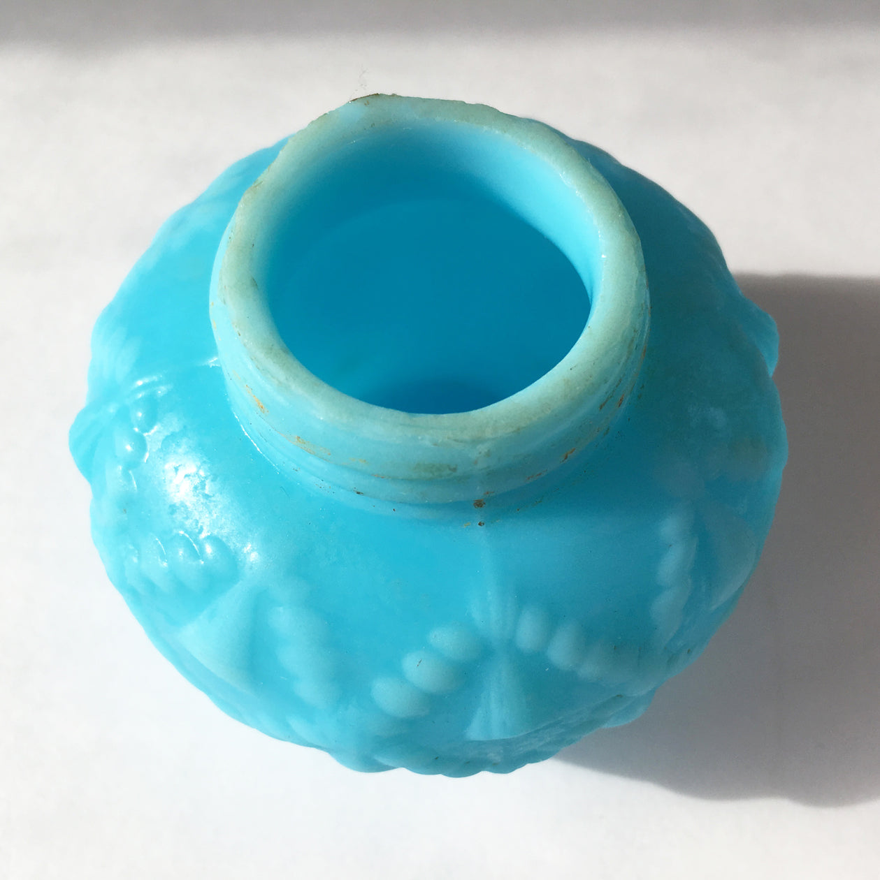 Overtop the mouth of a blue milk glass, Cord and Tassel, salt shaker without lid.