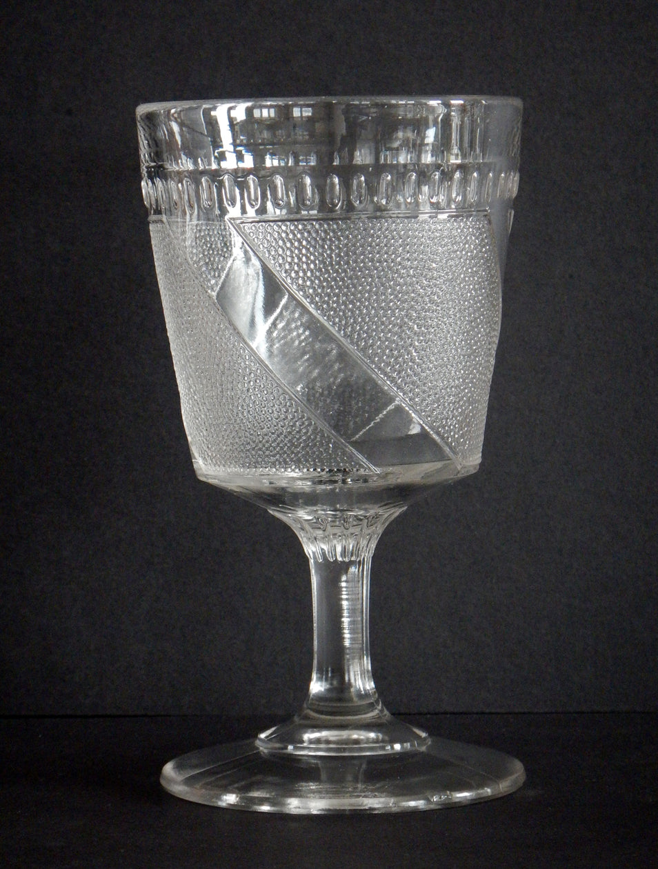 Close-up diagonal band and details on a clear pattern glass goblet.