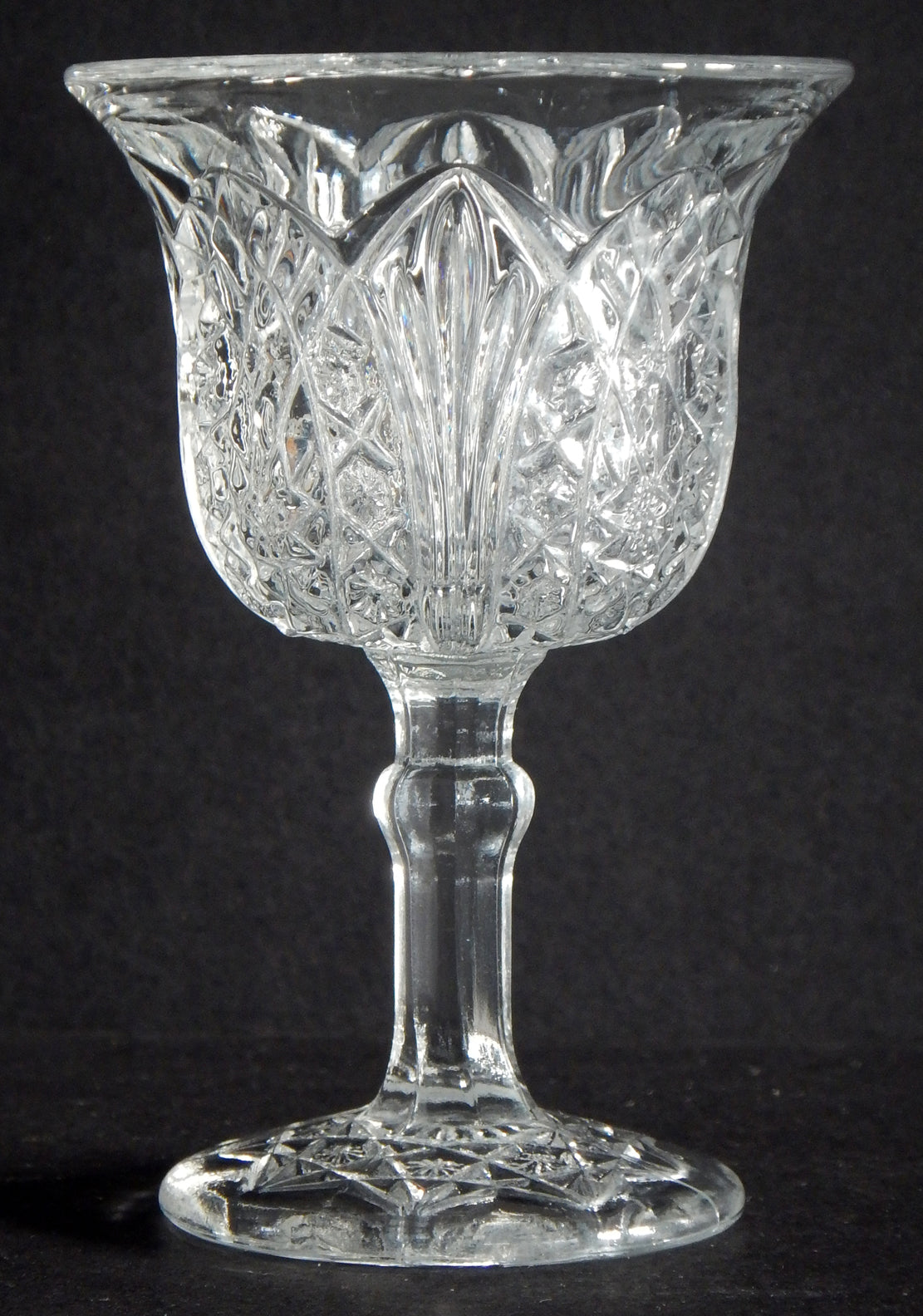 Close up of antique flared clear glass cordial with arrowhead style design.