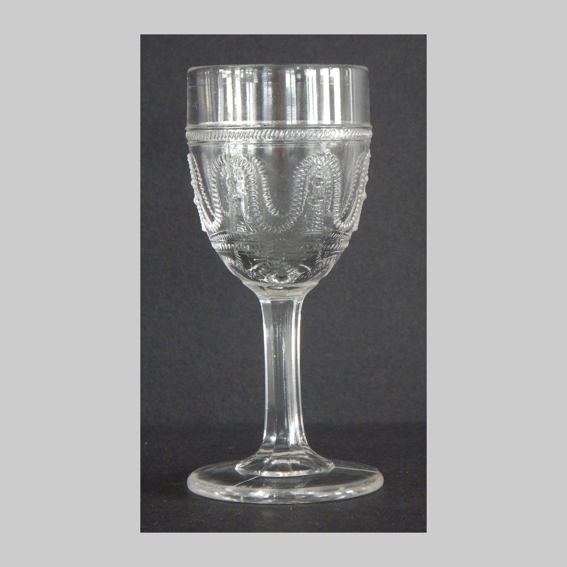 Antique clear glass cordial with cord and tassel pattern on the sides.