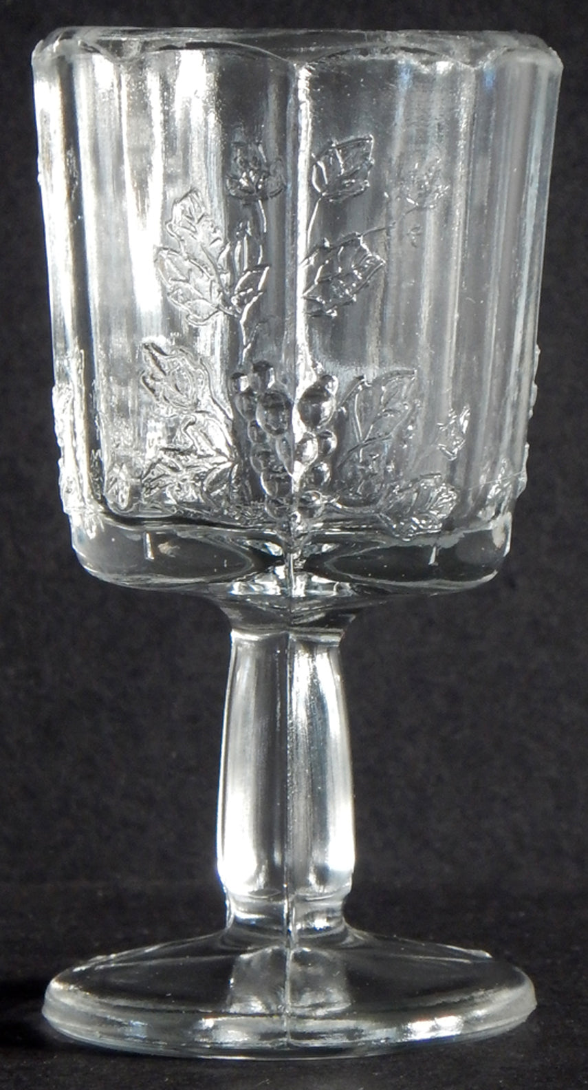 Close-up of seem of antique clear glass cordial with panels of grapes, vines, leaves.