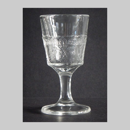 Antique clear pressed glass cordial with floral design and arches.