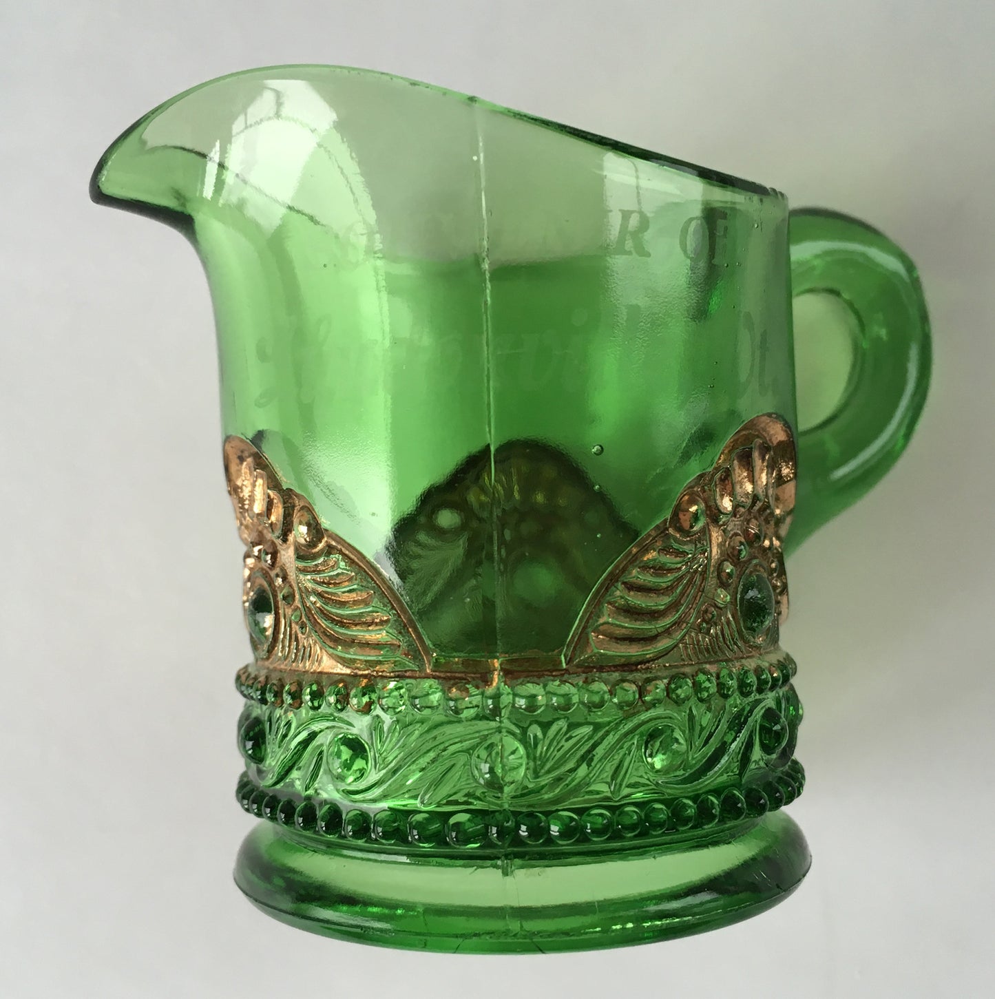 Close-up of seam on green pressed glass creamer with gold scallops.