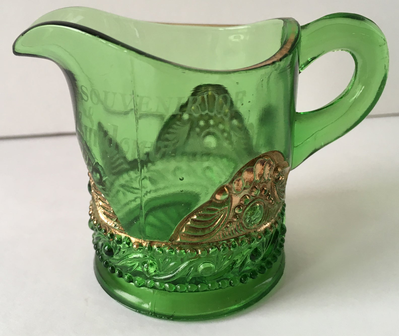 Close-up of green pressed glass creamer with gold bejewelled scallops pattern.