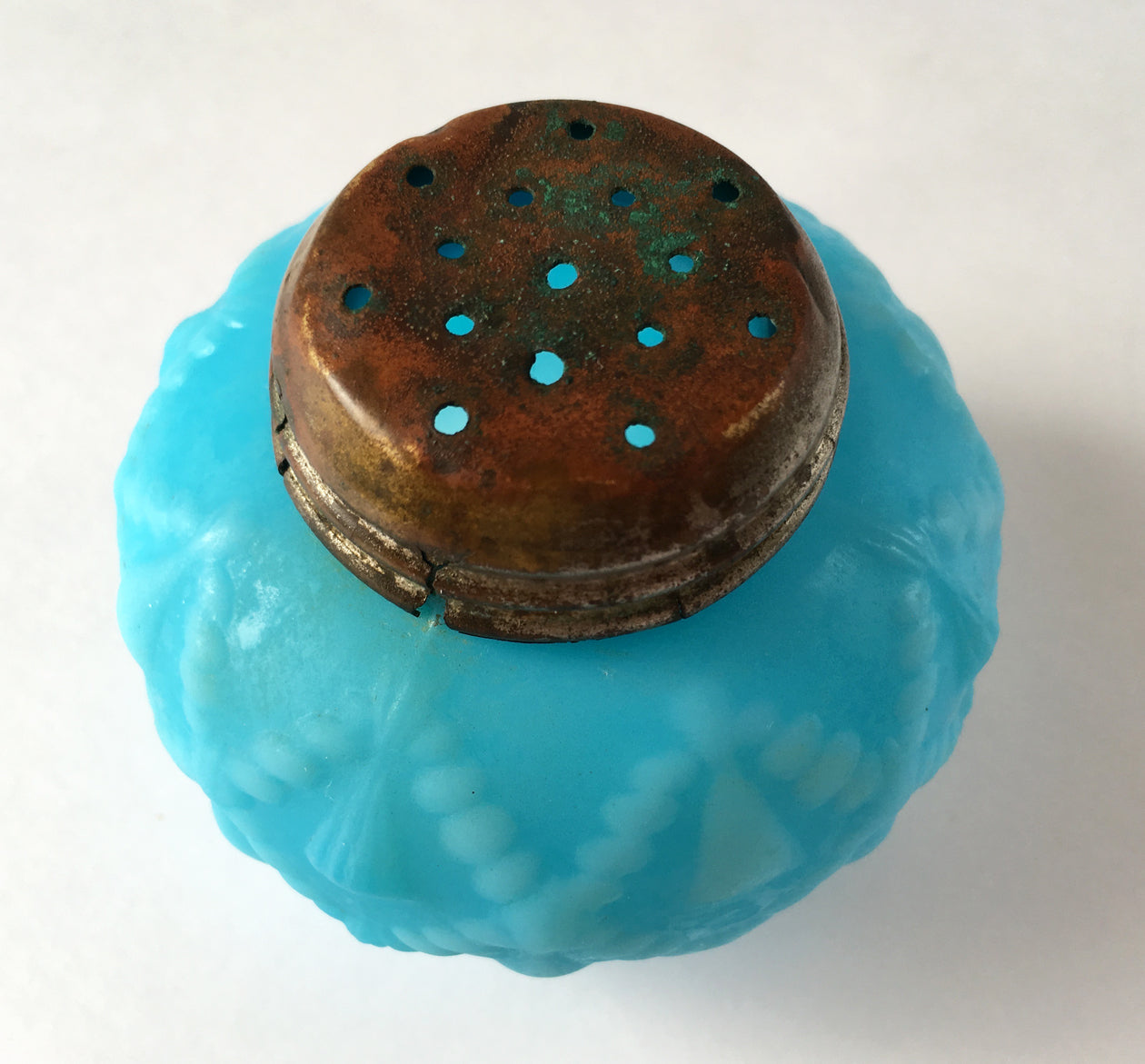 Overtop of an antique blue milk glass salt shaker and lid cords, tassels in pattern.