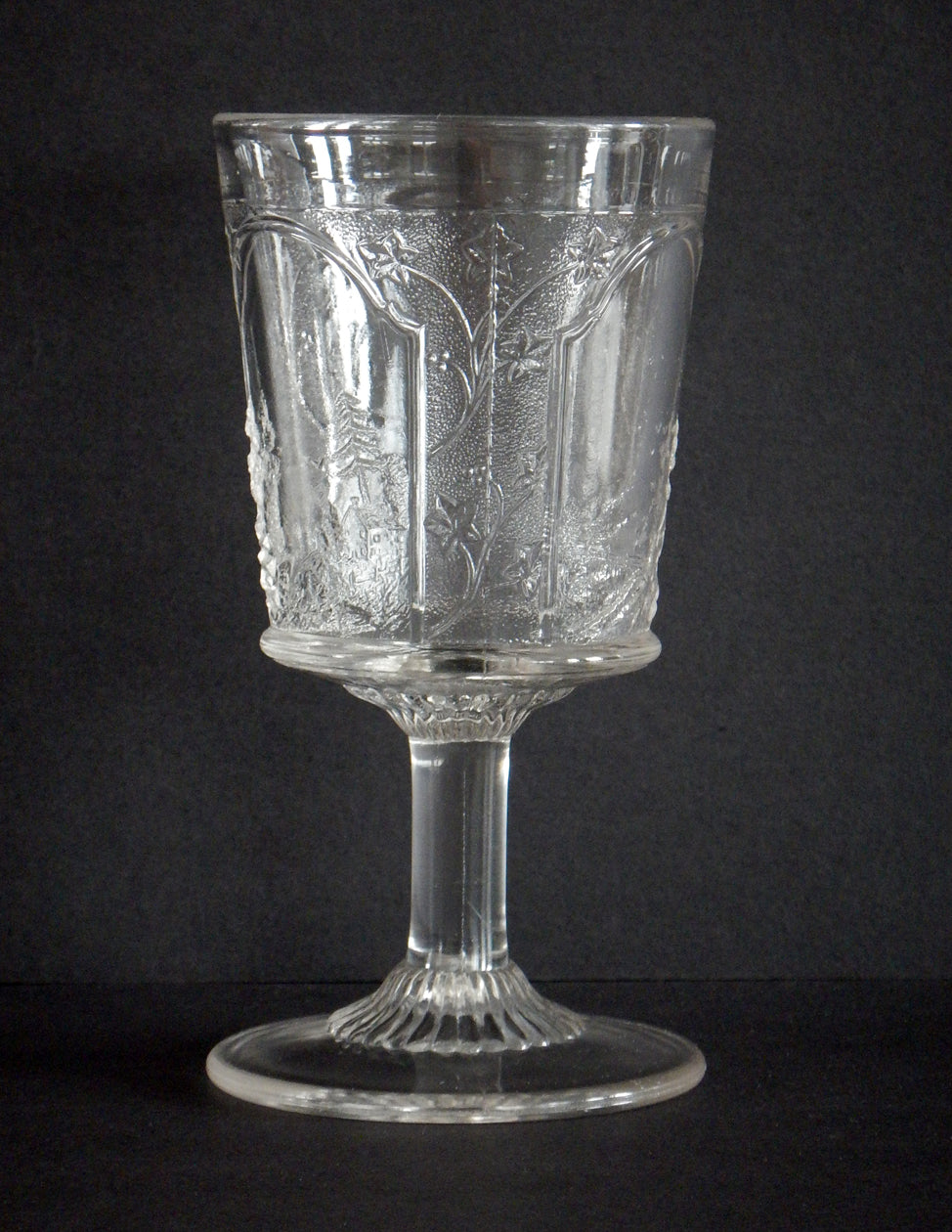 Close-up of leaves and countryside on a pressed glass goblet in Canadian pattern. 