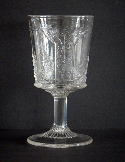 Close-up of leaves and countryside on a pressed glass goblet in Canadian pattern. 