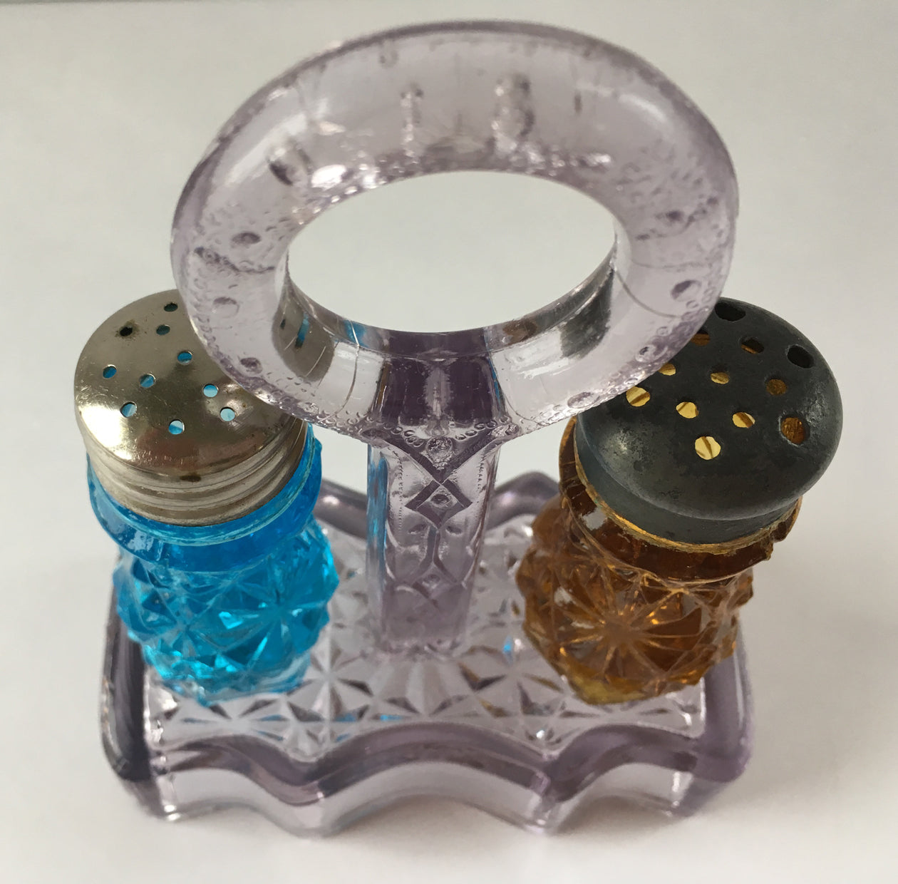 Above view of an antique pressed glass salt and pepper shakers and holder in colours.